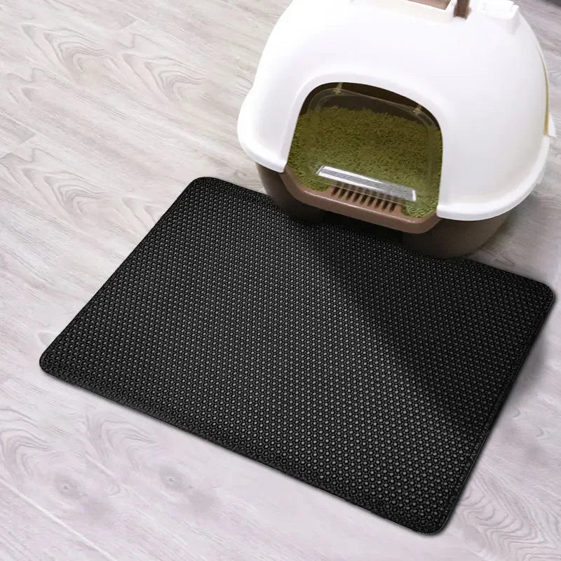 Black mat in front of a cat litter box on a light wooden floor
